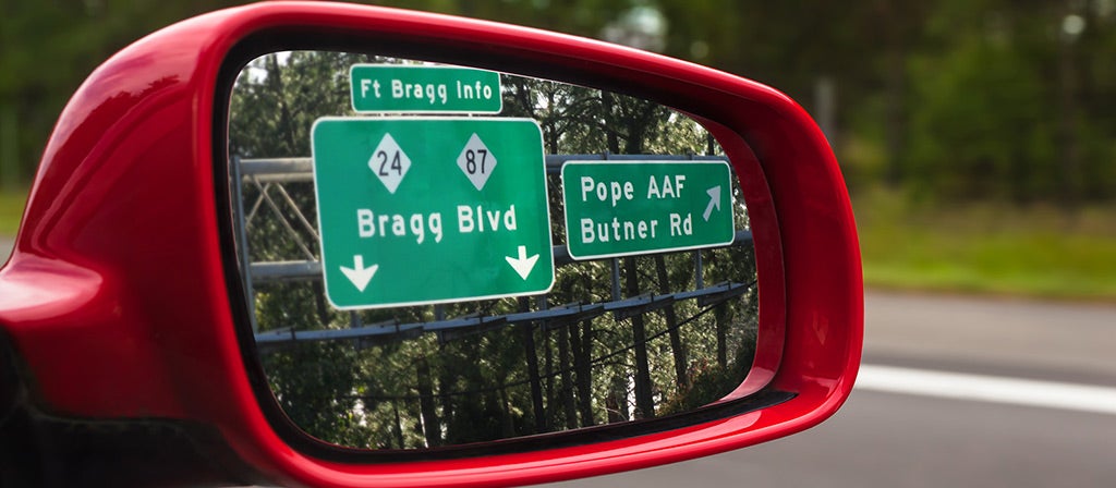 Road signs visible in the side mirror of a vehicle during a PCS.