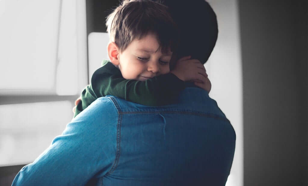 A picture of a child hugging his Dad's neck and smiling.