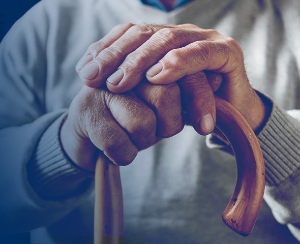 Close-up of an older adult’s hands resting on a wooden cane.