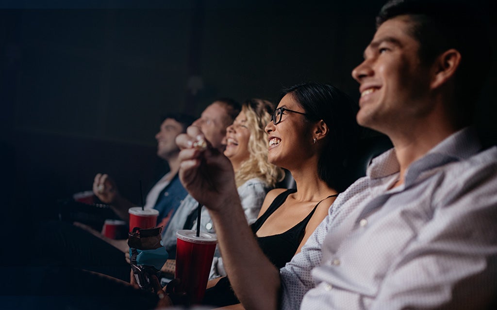 Photo of a row of patrons in a movie theater with popcorn