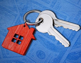 keyring with 2 keys and a house keychain laying over a blue background with dollar bill images overlaid
