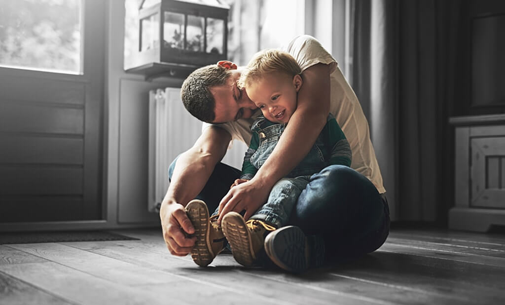 A father sitting on the floor and playing with his child in his lap