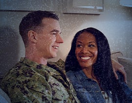 service member and their partner sitting closely on a couch, smiling