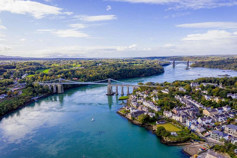 Aerial view of the Menai Suspension Bridge, foreground, and the Britannia Bridge, background, with the town of Menai Bridge, Anglesey, on the right, recent photograph (visitanglesey.co.uk)