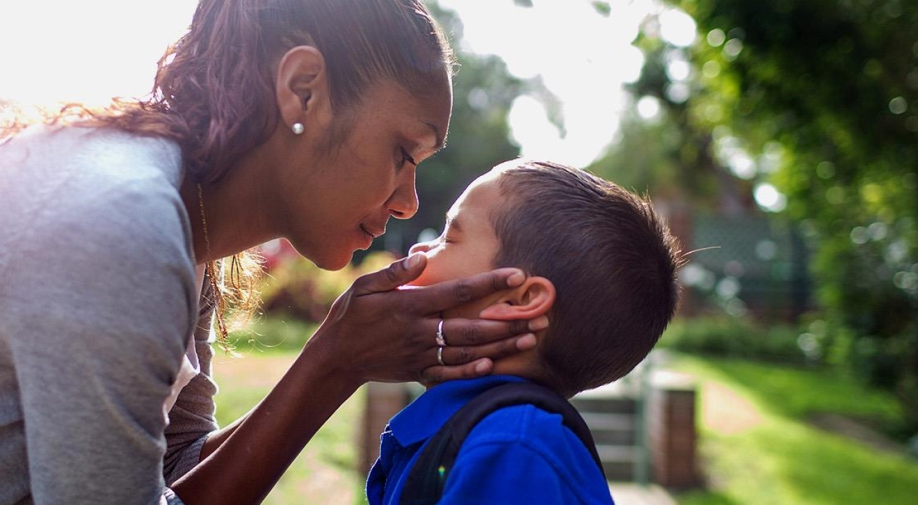 Indigenous woman holding young sons face in her hands