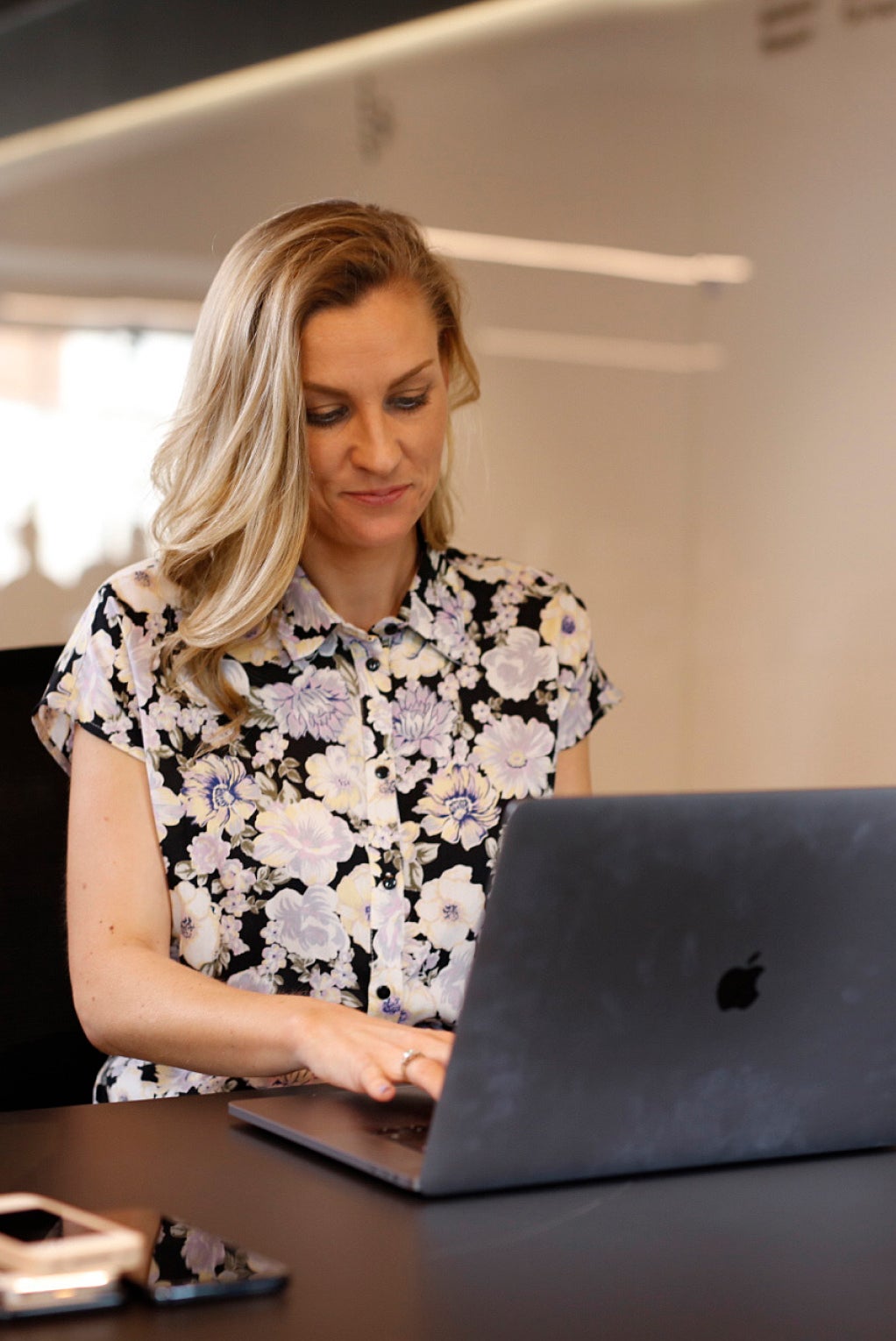 An individual in a flowery top is sitting down at a desk and working on their laptop.