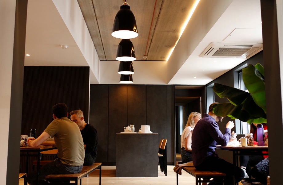 Individuals sitting down at two separate tables in the kitchen while they talk and have their lunch.