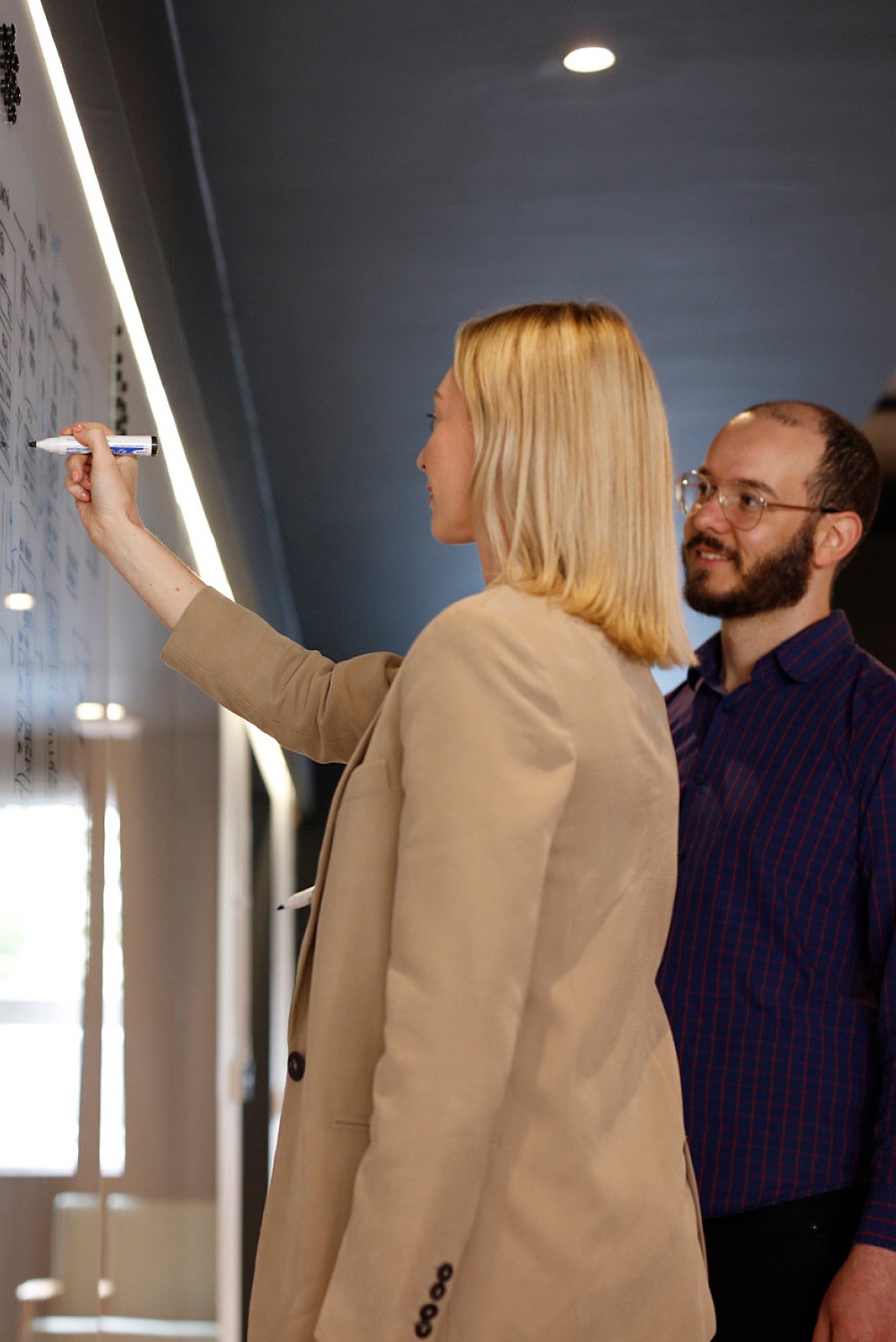 Two individuals are looking at the whiteboard and solving problems. The individual in the foreground is writing on it.